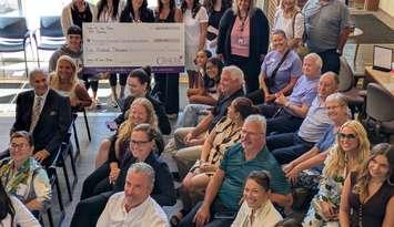 Press conference attendees, including John Viecelli (far left, in suit), and Carson Woodall of the Windsor Spitfires (in ball cap), show off a $500,000 cheque raised by the Windsor Cancer Centre Foundation's Show Us Your Brave campaign, July 22, 2025. Photo by Mark Brown/WindsorNewsToday.ca.