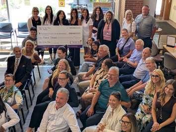 Press conference attendees, including John Viecelli (far left, in suit), and Carson Woodall of the Windsor Spitfires (in ball cap), show off a $500,000 cheque raised by the Windsor Cancer Centre Foundation's Show Us Your Brave campaign, July 22, 2025. Photo by Mark Brown/WindsorNewsToday.ca.